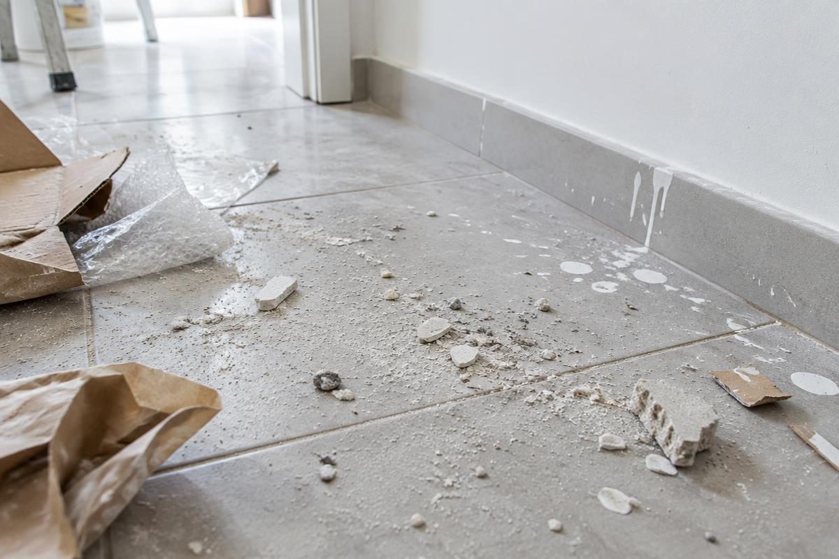 Poussières de plâtre, débris et éclaboussures de peinture sur un sol après travaux